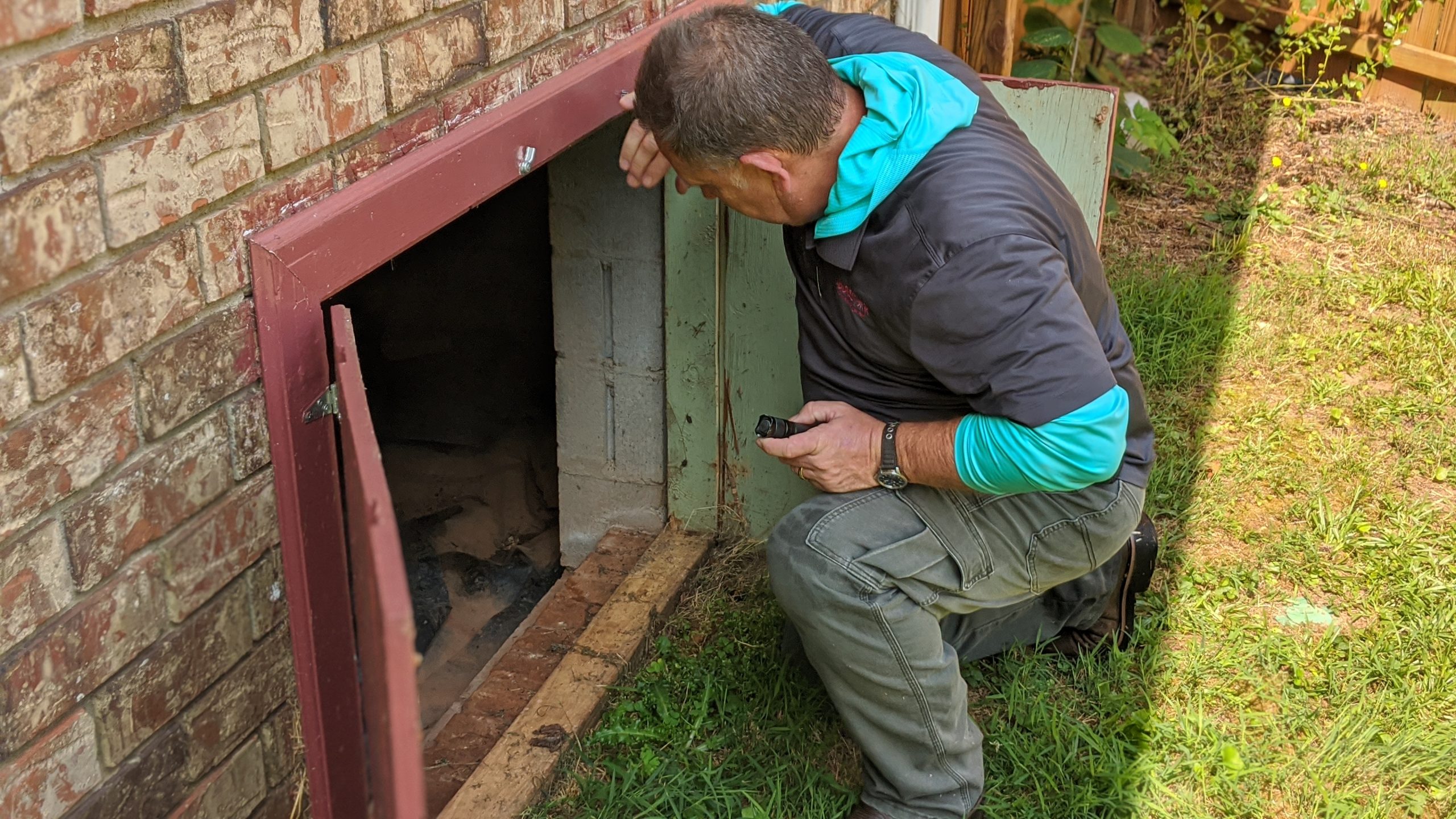 Pest Control Technician looking for signs of pest infestation in crawlspace entrance