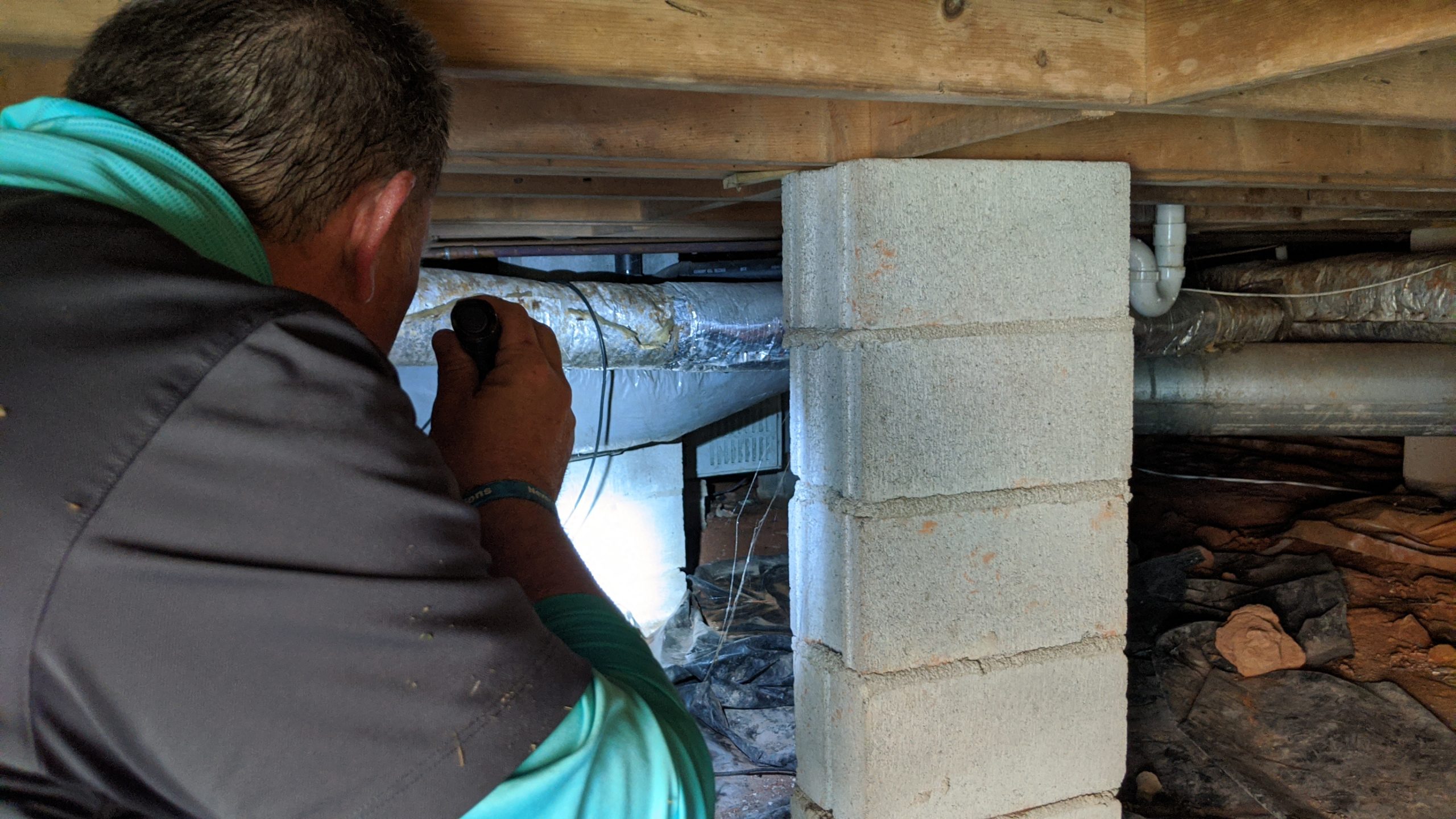 picture of a man crawling under a home pointing a flashlight